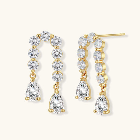 Gold-plated earrings with vertical line of clear crystals and teardrop pendants on neutral background